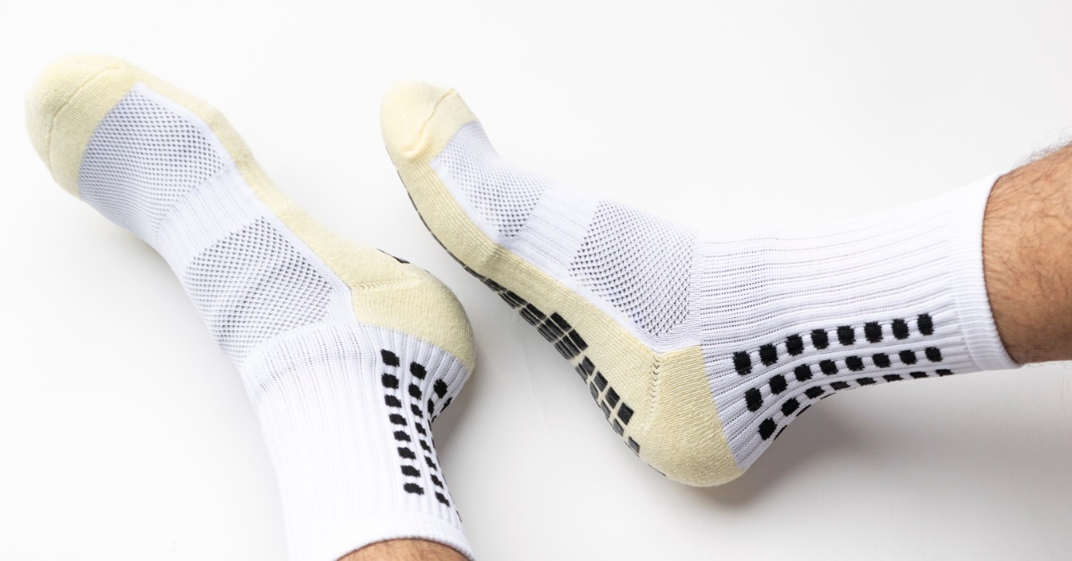 A pair of feet wearing white athletic grip socks with black rubber traction pads and pale yellow toes and heels.